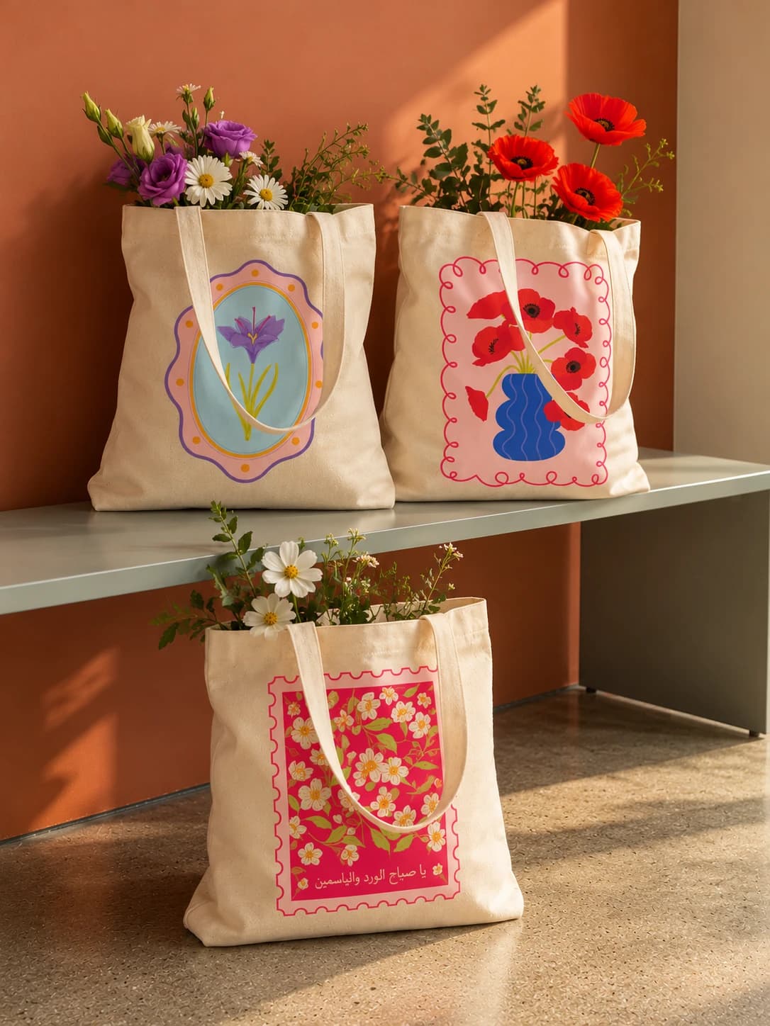 Three canvas totes with colorful floral and poppy prints, filled with fresh flowers, against a terracotta wall